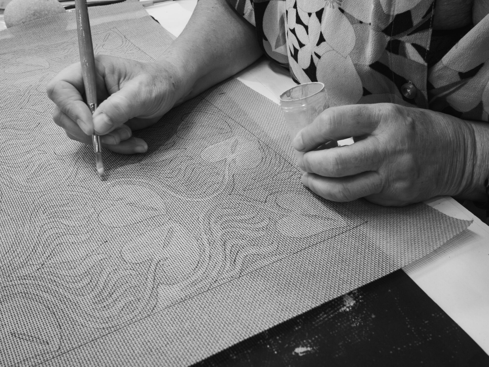 Woman's hand holding a paint brush and painting a pattern on fabris